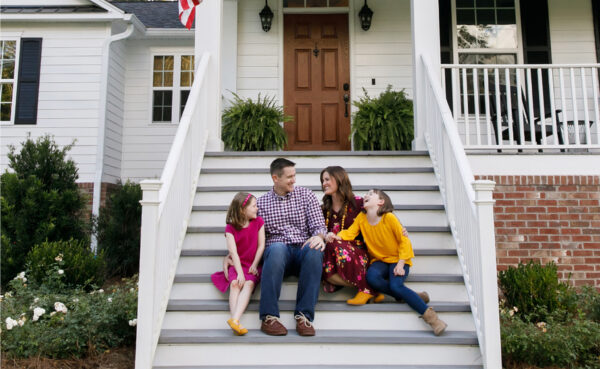 A happy family sitting on the staircase in front of their home, laughing and enjoying each other's company.