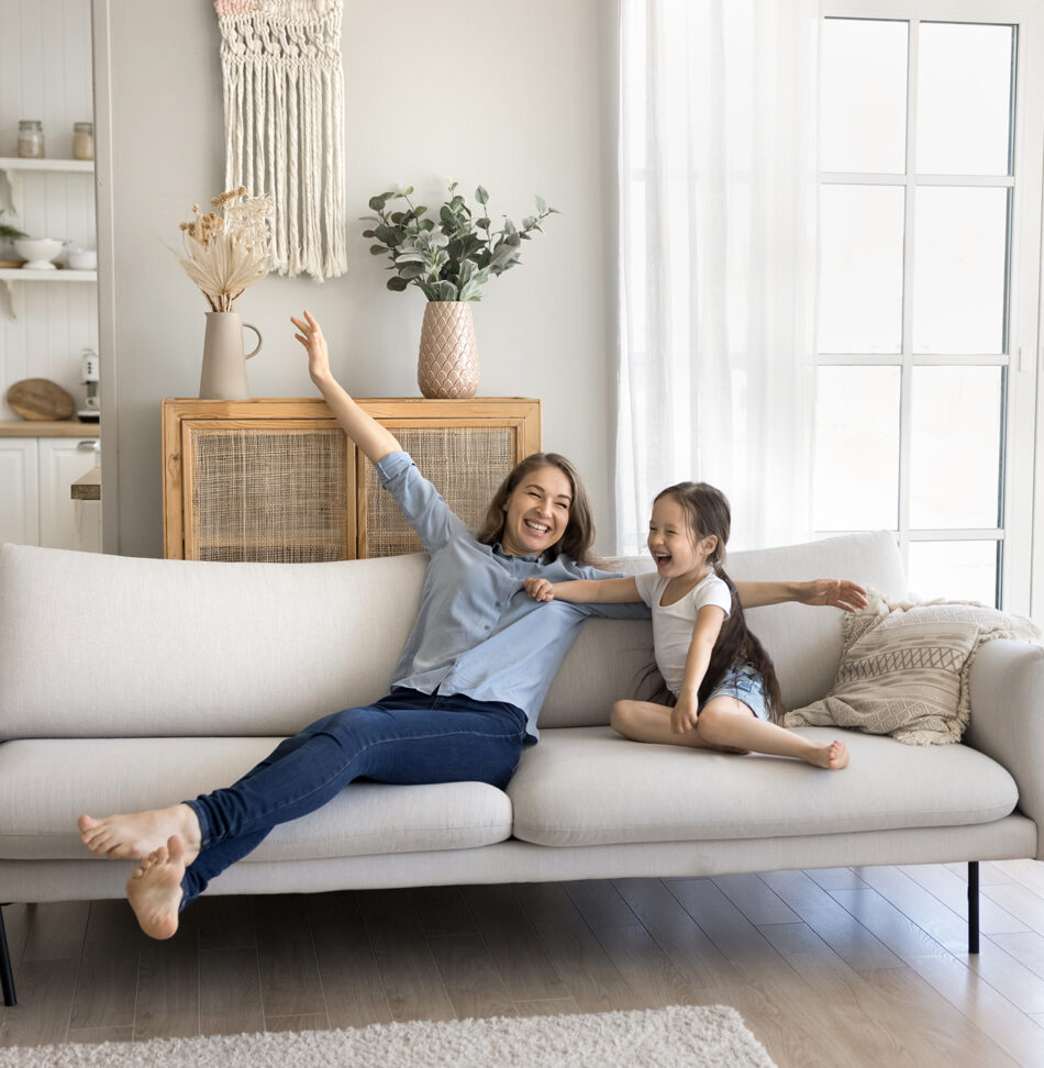 A mom and daughter enjoying their clean home by Professional Edge Cleaning, stretched out and laughing on the cough.