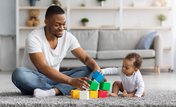 A Dad and a baby playing blocks on a clean carpet.