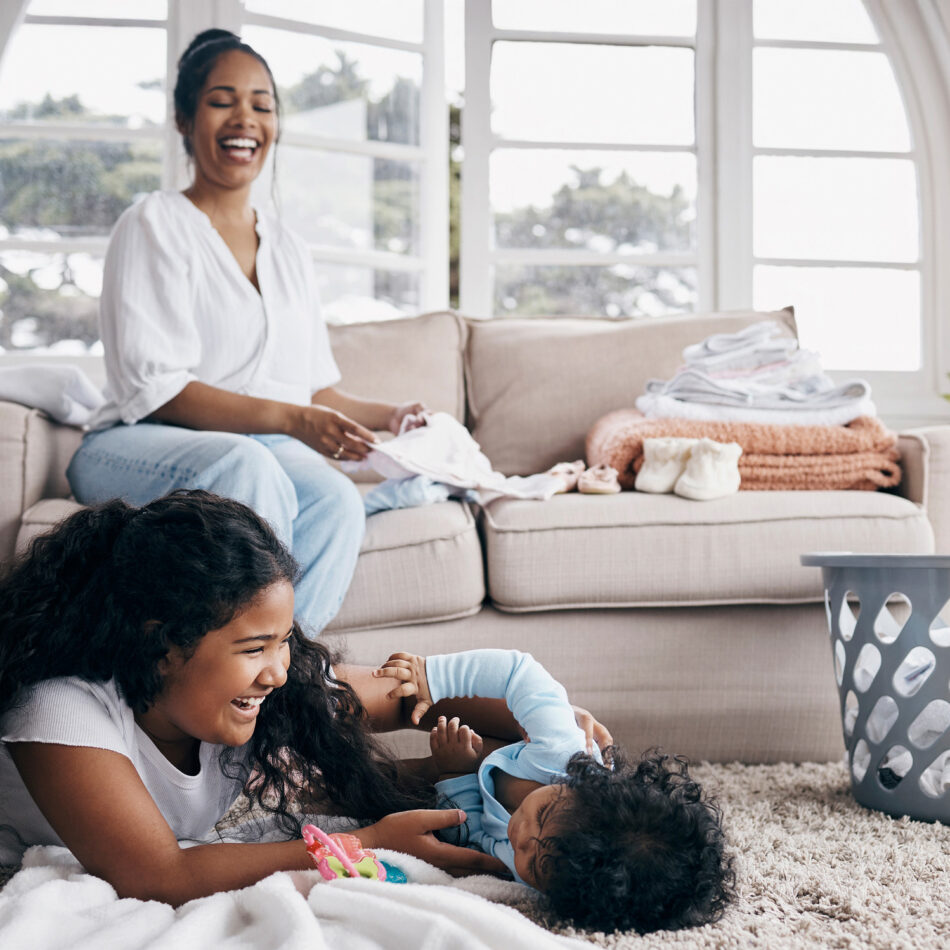 A Mom and her two kids, the Mom doing laundry while the two kids play on the fresh carpet provided by house cleaning services with Professional Edge Cleaning.